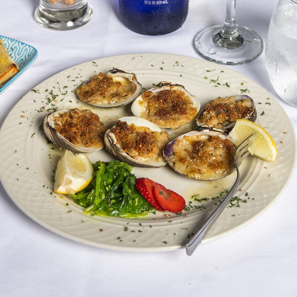 Baked clams with breadcrumbs, lemon, seaweed salad, and sliced strawberries on a white plate.