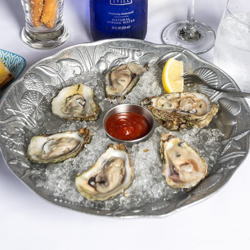 Six fresh oysters on a bed of ice with cocktail sauce and lemon, alongside garlic bread.