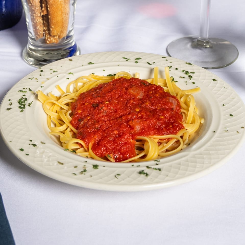 A white plate of linguine pasta topped with chunky red marinara sauce and parsley flakes.