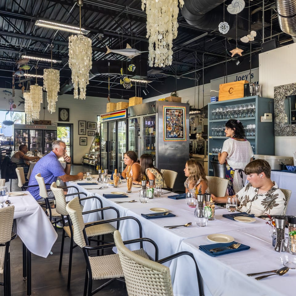 Diners seated at white-clothed tables in a restaurant with nautical decor and a server.