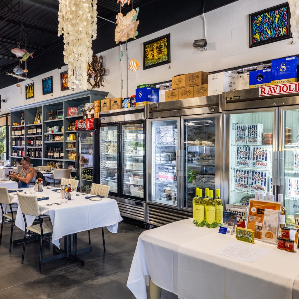A restaurant interior with dining tables, display refrigerators, and shelves stocked with wine and food items.