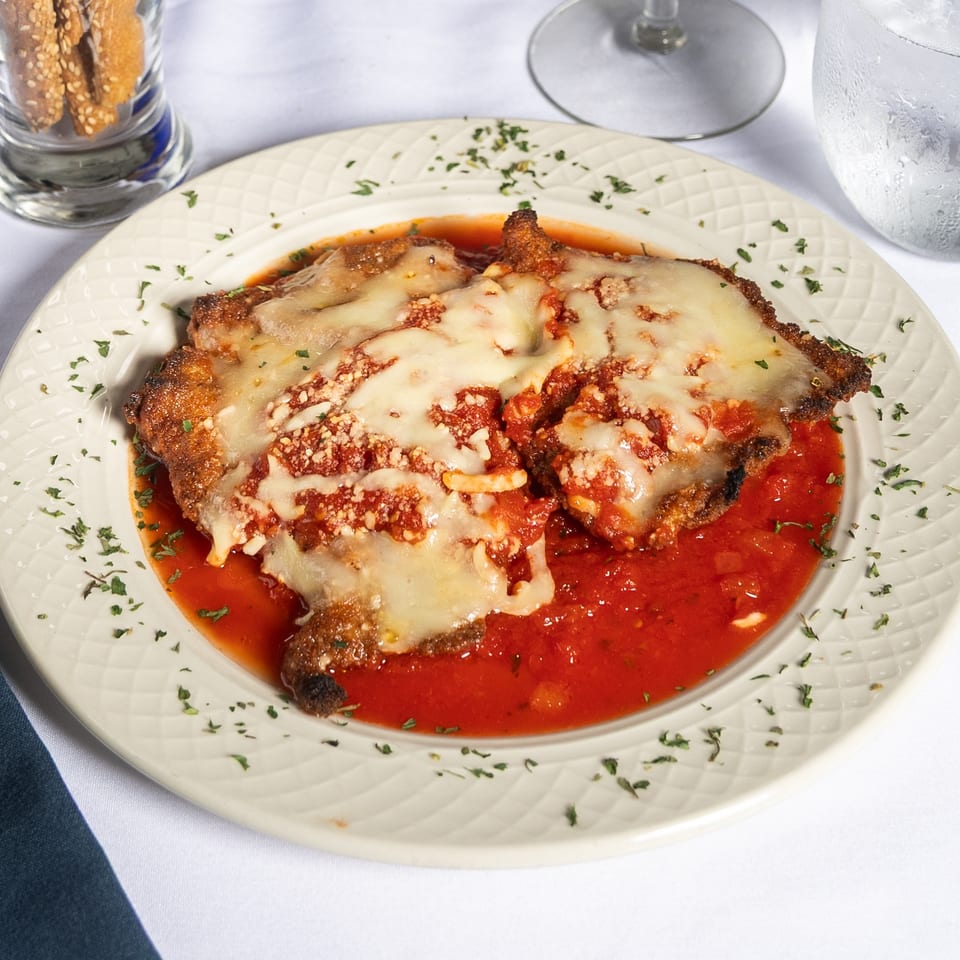 Chicken parmesan with melted cheese and red sauce, garnished with parsley on a white plate.