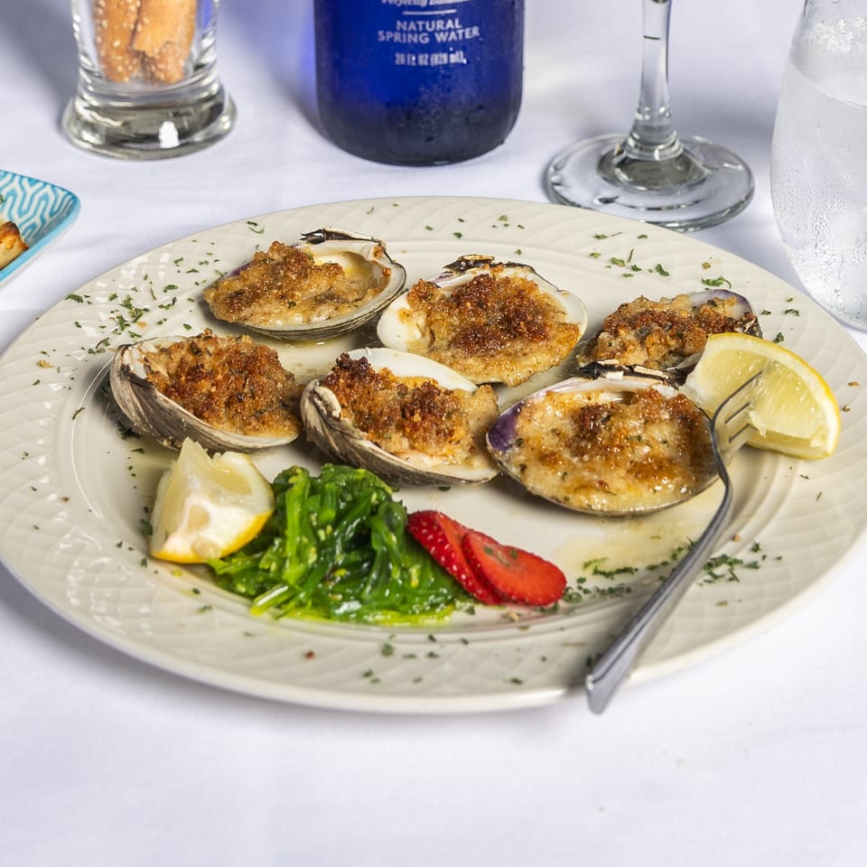 Baked clams with breadcrumbs, lemon, seaweed salad, and strawberries on a white plate.