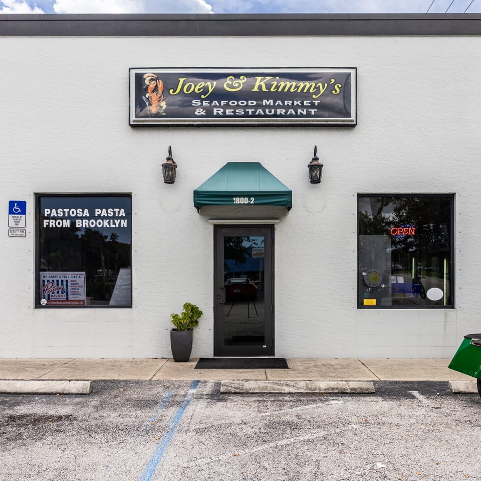 Exterior of Joey & Kimmy's Seafood Market & Restaurant, a white building with a green awning and sign.