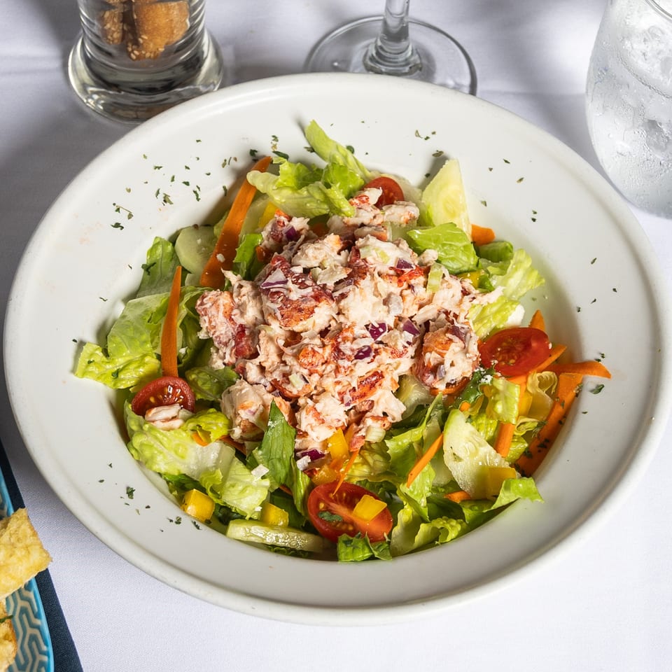 A fresh lobster salad with mixed greens, tomatoes, and cucumbers, served with garlic bread.