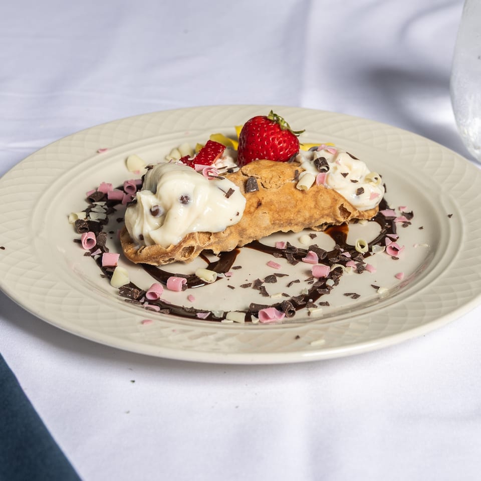 A cannoli dessert with cream, chocolate shavings, and strawberries on a white plate.